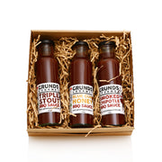 Three bottles of Grunds Gourmet BBQ sauce in a decorative box with straw-like filler on a white background.