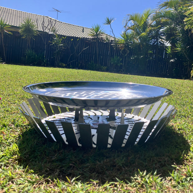 Reflective metal object on grass with blue sky and trees in the background