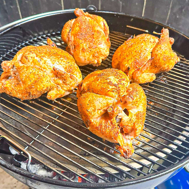 Four seasoned chickens on a grill