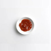 Small white bowl with red sauce on a light gray background