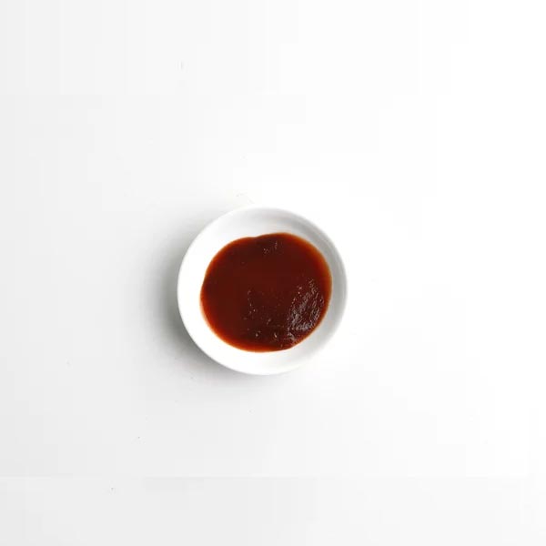 Small white bowl filled with dark red sauce on a light gray background